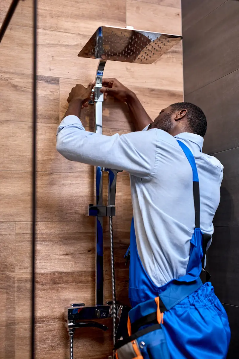 Plumber in blue overalls adjusting pipes in a modern bathroom setting.