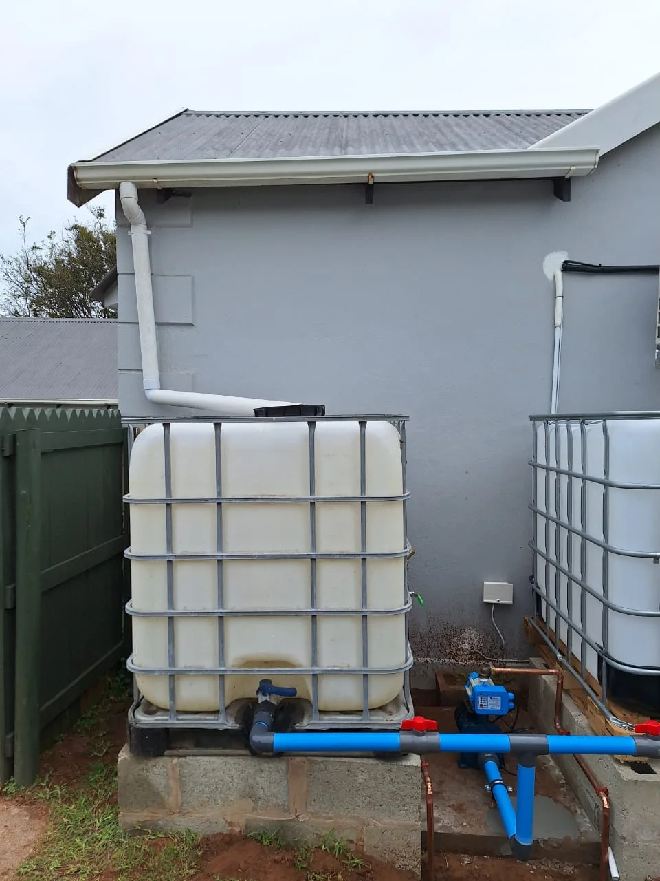 Exterior view of a large water tank connected to a residential plumbing system.